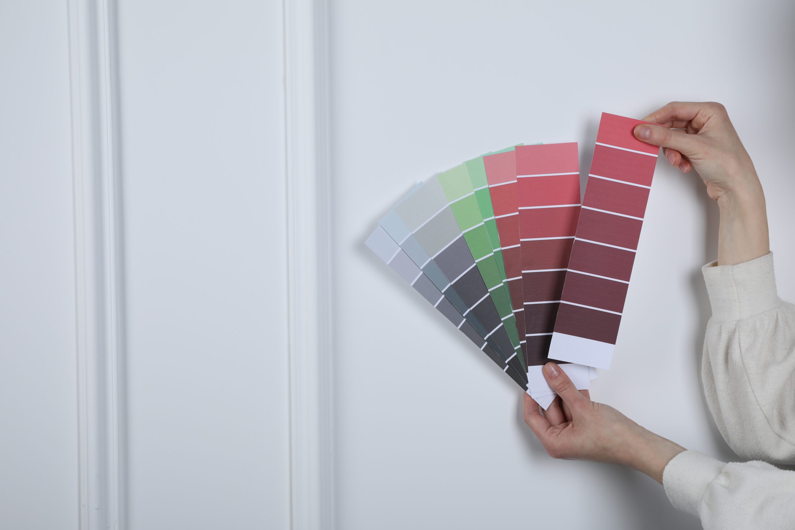 Woman with paint chips choosing color near white wall, closeup. Interior design
