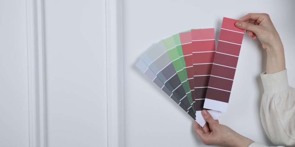 Woman with paint chips choosing color near white wall, closeup. Interior design